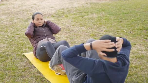 Deux séances d'entraînement à l'extérieur. Les jeunes couples latino-américains s'assoient ensemble sur un tapis jaune commun dans un parc pluvieux d'automne dans le cadre d'un programme de routine d'entraînement . — Video