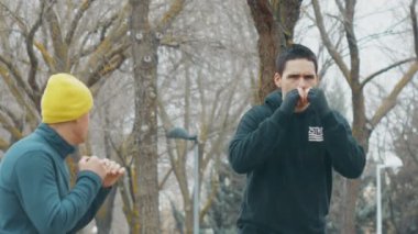 Boks egzersiz ile eğitmen açık havada. Beyaz delikanlı siyah hoodie pratik gölgede yağmurda Delme. Sarı örgü kap ile Koç kaçmak öğretir.