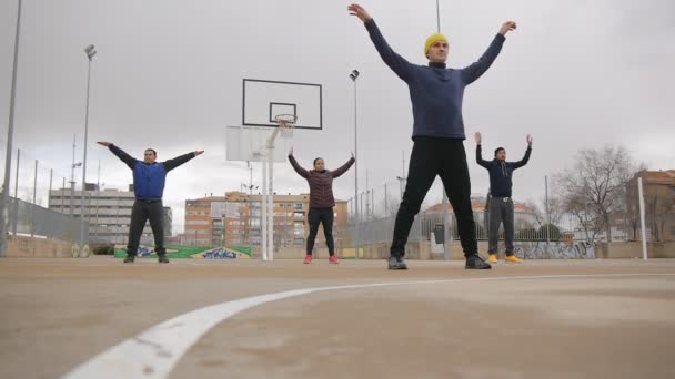 Entrenamiento callejero. Tiro de bajo ángulo del grupo deportivo de jóvenes multiétnicos que practican tai chi o qigong en la cancha de baloncesto al aire libre como parte de una rutina de entrenamiento . — Vídeo de stock