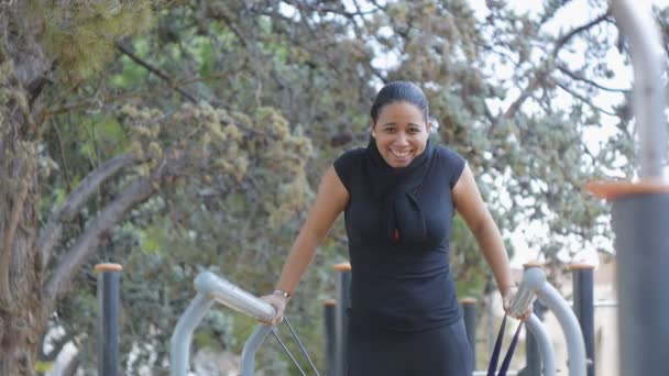 Treino de rua. Jovem mulher latino-americana falha em cair da banda de resistência com medo de tentar fazer mergulhos de bar no ginásio fitness ao ar livre no parque. A menina ri com surpresa . — Vídeo de Stock