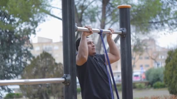 Οδός προπόνηση προπόνηση. Cross fit άνθρωπος κάνει pull-ups με αντίσταση μπάντα στο υπαίθριο γυμναστήριο στο πάρκο. — Αρχείο Βίντεο