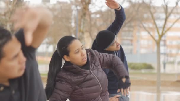 Entrenamiento callejero. Grupo deportivo de tres jóvenes étnicos haciendo ejercicio de alcance lateral en el parque de otoño bajo la lluvia como parte de una rutina de entrenamiento . — Vídeo de stock