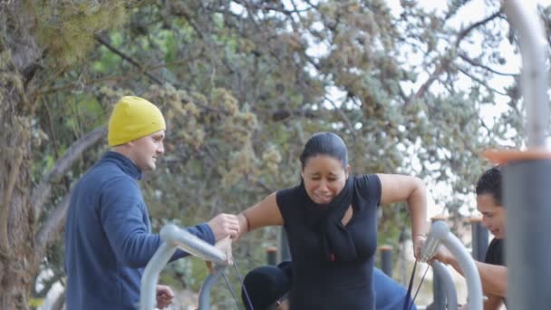 Entrenamiento callejero. Mujer hispana tomando posición inicial en barra paralela con la ayuda de tres personas en gimnasio al aire libre en el parque . — Vídeos de Stock