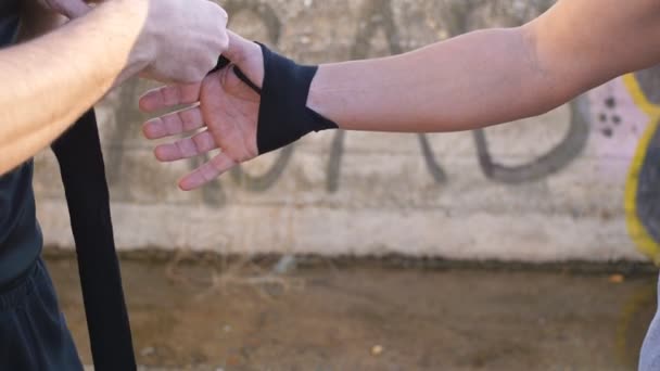 Entrenamiento con entrenador personal al aire libre. Manos masculinas envolviendo el vendaje elástico deportivo negro en el brazo de los deportistas . — Vídeo de stock