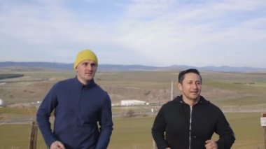 Kişisel antrenör açık havada ile egzersiz. İki adam bir ülke yolunda ağır çekimde dağlık arazi arka plan üzerinde sonbahar veya ilkbahar koşu.
