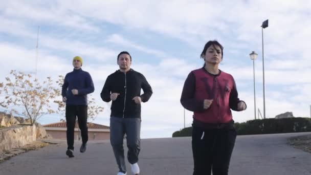 Entrenamiento con entrenador personal al aire libre. Dos hombres y una mujer corriendo por el camino en cámara lenta en otoño o primavera . — Vídeo de stock