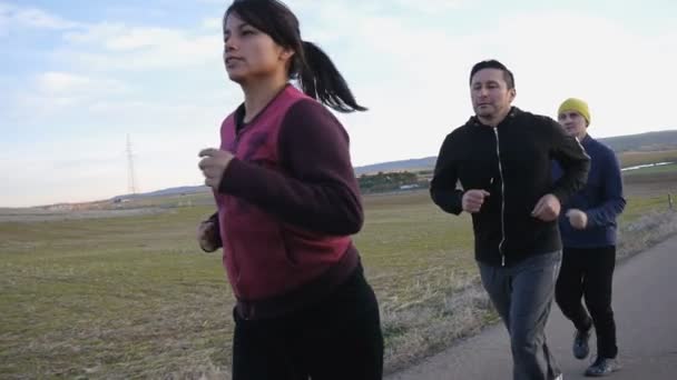 Cvičení s osobním trenérem venku. Dva muži a žena běží po jednom na venkovské silnici v na podzim nebo na jaře. — Stock video