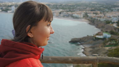 Genç kadın deniz arka plan üzerinde. Yakın çekim kırmızı kapüşonlu sahil seyir içinde gülümseyen beyaz kahverengi saçlı kadın portresi.