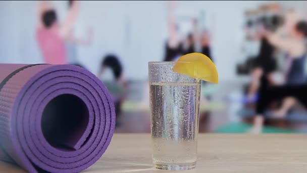 Caída de una rebanada de limón en un vaso con agua, yoga, pilates, empleo en grupo por deportes — Vídeo de stock