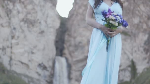 Meisje in een jurk met een boeket op de achtergrond van een waterval — Stockvideo