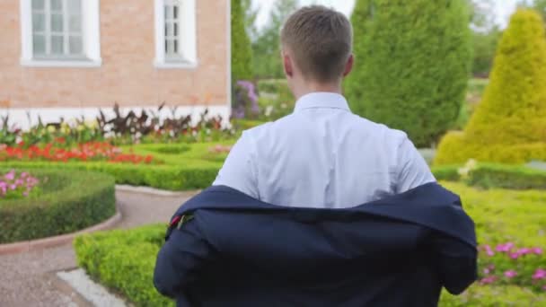 Joven vistiendo una chaqueta de traje en un hermoso jardín lento mo — Vídeos de Stock