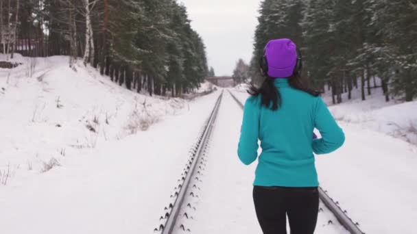 Девочка зимой бегает среди деревьев по железной дороге — стоковое видео