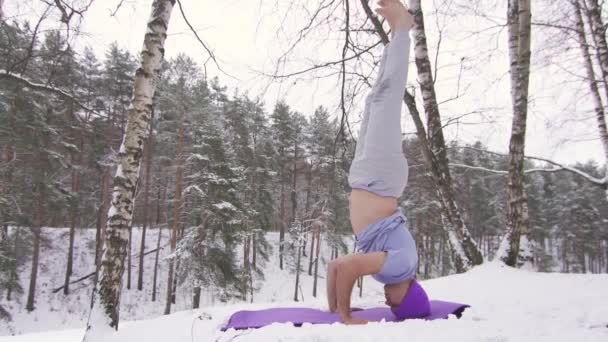 Un hombre en un bosque de invierno hace una parada en su cabeza, esterilla de yoga — Vídeos de Stock