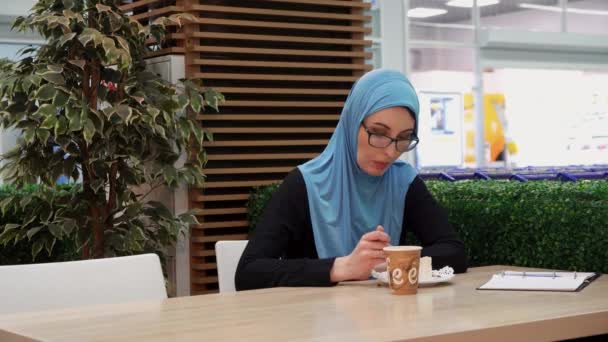 Мусульманська дівчинка в окулярах в кафе п'є каву і їсть — стокове відео