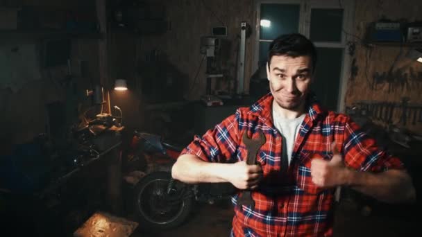 Mécanicien masculin dans une chemise montre pouce vers le haut sur le fond des étagères avec des outils dans le garage — Video