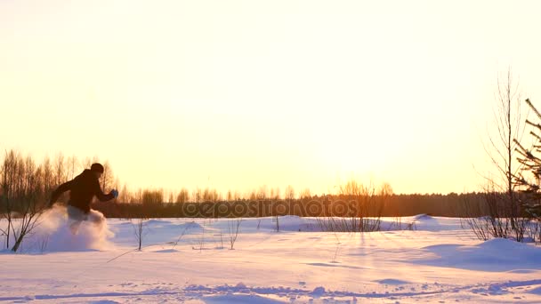 Мужской силуэт бежит по глубокому снегу на закате солнца зимой — стоковое видео