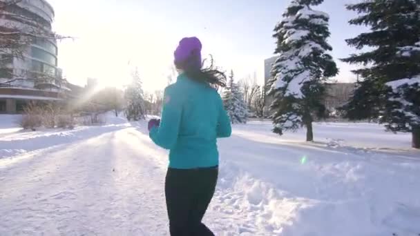 Una chica en invierno corre por la ciudad en invierno en un día soleado — Vídeos de Stock