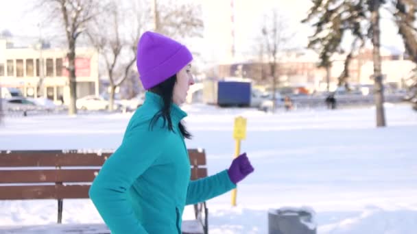 Brunett tjej jogging på en solig vinterdag i staden på en bilar bakgrund, långsamma mo — Stockvideo