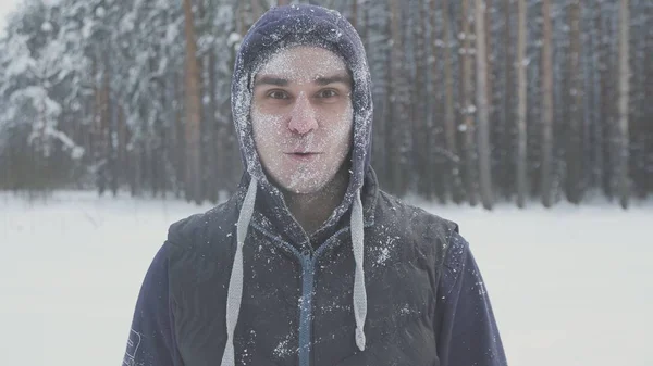 Удивленный замерзший мужчина в очках в снегу смотрит в камеру в зимнем лесу после снежной бури — стоковое фото