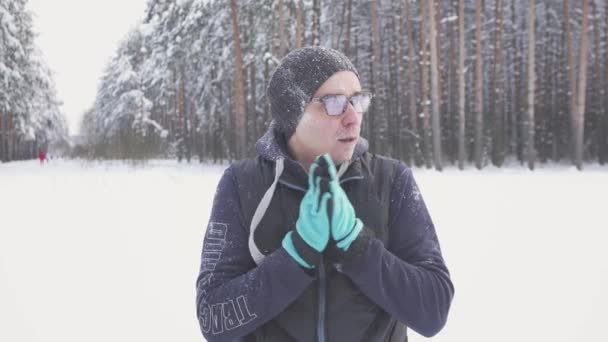 Hombre congelado en el frío con gafas en el parque de invierno, frotándose las manos, heladas — Vídeo de stock