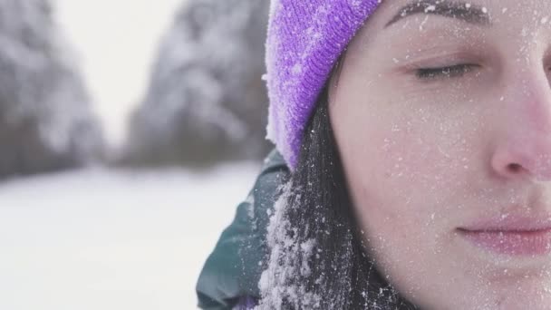 Девушка в фиолетовой шляпе смотрит в камеру на фоне зимнего леса, иней — стоковое видео