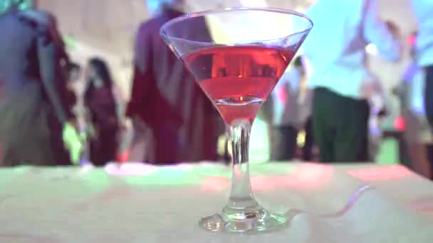 Bicchiere solitario con alcol sullo sfondo di persone che ballano — Video Stock