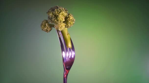Broccoli op een vork op een groene achtergrond, rotatie — Stockvideo