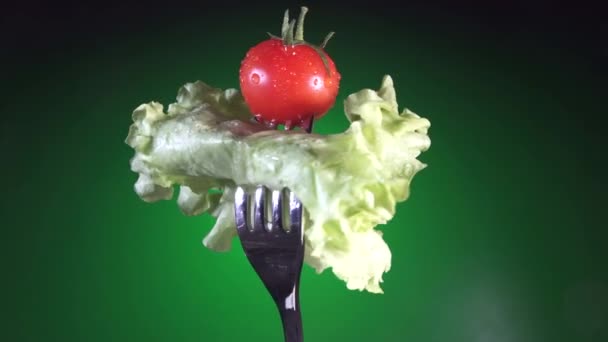 Tenedor con tomate rojo fresco en gotitas de agua y lechuga rota fondo verde — Vídeo de stock