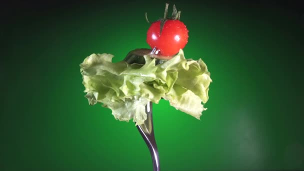 Fork with fresh red tomato and cucumber in water drops and lettuce rotates green background — Stock Video
