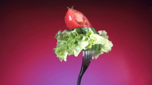 Tenedor con tomate y pepino en rodajas rojas frescas en gotas de agua y lechuga rota fondo rojo — Vídeos de Stock
