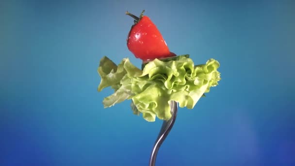 Tenedor con tomate rojo fresco y pepino cortado en gotitas de agua y lechuga gira fondo azul — Vídeo de stock