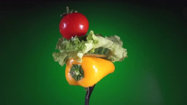 Gabel mit gelben Paprikascheiben von Gurken, Radieschen und Salat dreht grünen Hintergrund — Stockvideo
