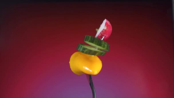 Tenedor con rodajas de pimiento amarillo de pepino y rábano, un fondo rojo gira — Vídeos de Stock