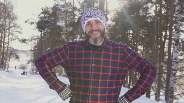 Портрет бородатого улыбающегося человека в зимнем лесу, смотрящего в камеру — стоковое видео
