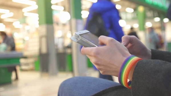 Chica adolescente con un símbolo de pulsera LGBT utiliza un teléfono en un centro comercial Imagen De Stock