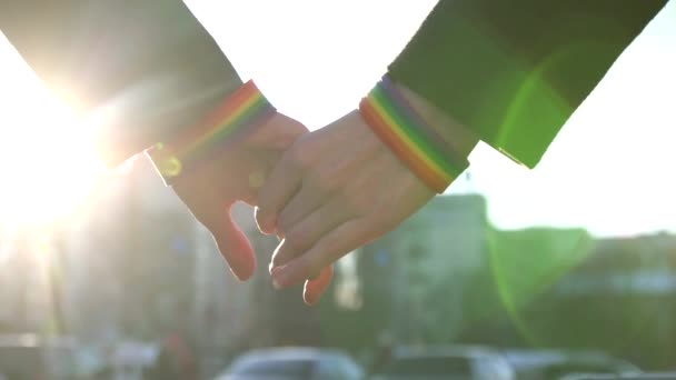 Two hands stretch to each other with LGBT bracelets against the backdrop of the street — Stock Video