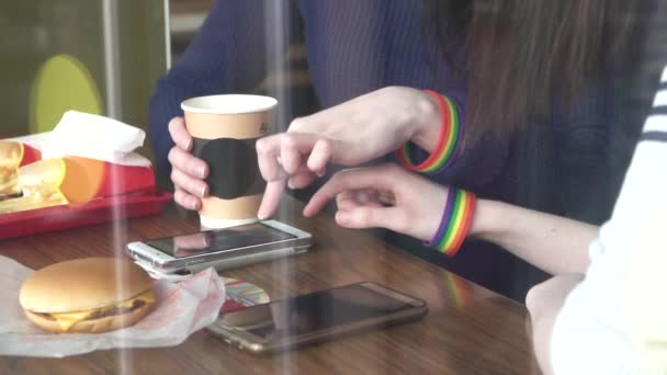 Mulheres mãos no café usando um telefone com pulseiras LGBT de perto — Vídeo de Stock