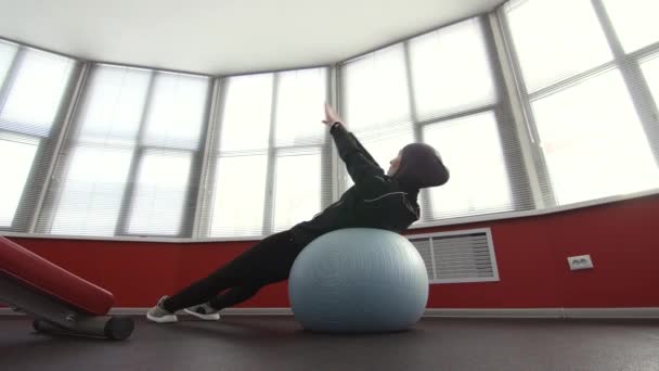Дівчина в хіджабі на фітнес-кулі в спортзалі сидить — стокове відео