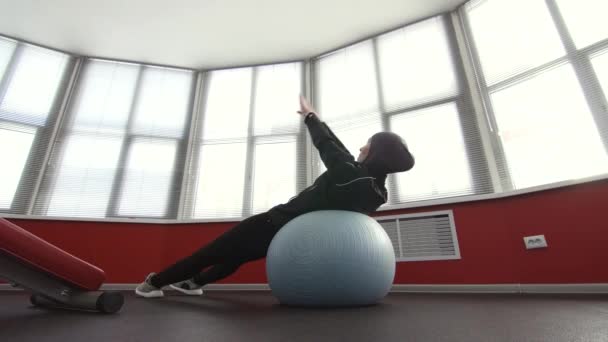 Mädchen im Hijab auf Fitnessball in Turnhalle sitzen — Stockvideo