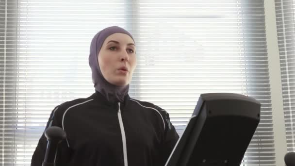 Retrato de una atleta con un hijab en un simulador de pasos en un gimnasio — Vídeos de Stock
