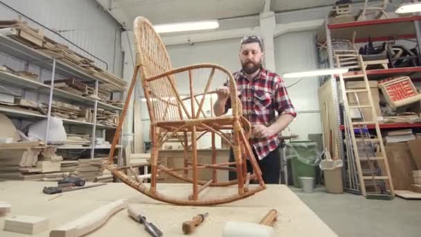 Man carpenter in a wooden workshop with a rocking chair — Stock Video