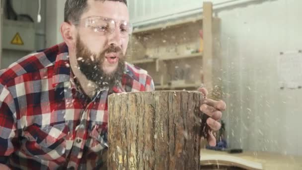 Чоловік столяр у сорочці з бородою дме стружку в майстерні — стокове відео
