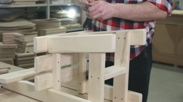 Carpintero trabajando en una camisa con barba en el taller hace una silla de madera — Vídeo de stock