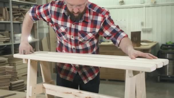 Тесля, що працює в сорочці з бородою в майстерні нагріває дерев'яну лавку — стокове відео