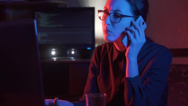 Девушка за компьютером разговаривает по телефону — стоковое видео
