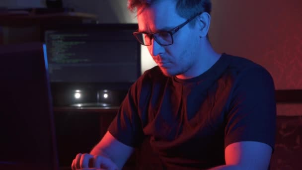 Portrait of a man in a dark room at a computer wearing glasses — Stock Video