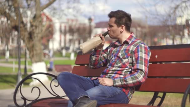 Uomo in camicia che beve alcol in un parco su una panchina — Video Stock