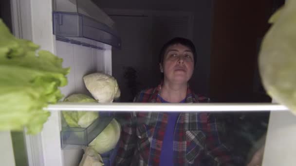 Nő 40 éves a diéta megnyitja a hűtőben, éjjel, és eszik egy saláta — Stock videók