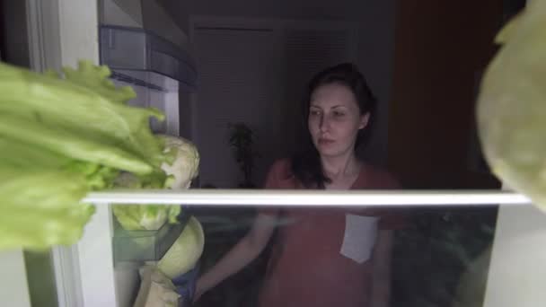 Sad girl opens the refrigerator at night and looks at the food on the diet — Stock Video