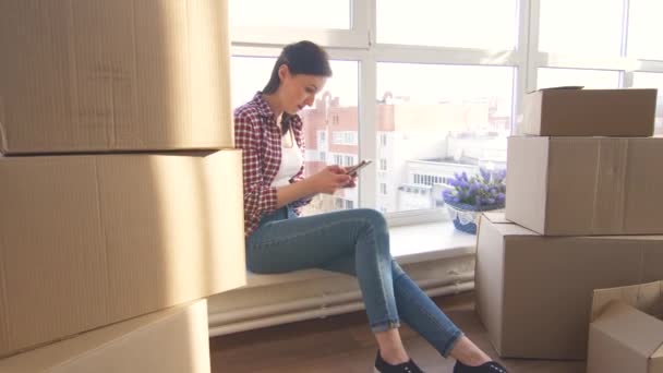 Mujer joven utilizado en el teléfono sentado en el nuevo apartamento de mudanza en — Vídeo de stock